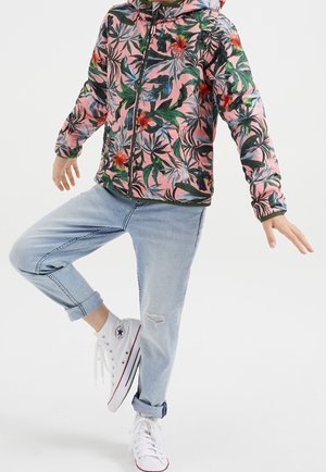 Różowa kurtka na suwak z kapturem w kwiatowy wzór; z zielonymi liśćmi i czerwonymi kwiatami. Połączona z jasnoniebieskimi dżinsami i białymi trampkami.