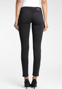 Jeans negros ajustados con textura suave, diseño de cinco bolsillos y parche con el logo en la cintura. Ajustados en la pierna para una silueta ceñida.