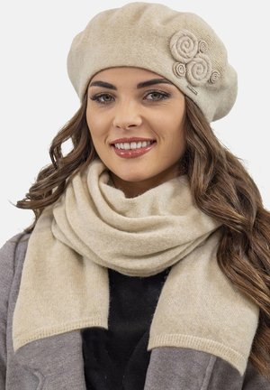 Berretto beige con tre dettagli di tessuto arrotolato, abbinato a una sciarpa beige coordinata, entrambi realizzati in materiale morbido e testurizzato.