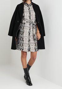 Cappotto nero su un vestito a fantasia con motivo in pelle di serpente bianco e nero. Stivali al ginocchio neri lucidi e una pochette come accessorio.