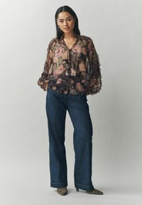 Permatomi juoda gėlėta bluzonė su rožinėmis ir žalios rožėmis, su raukšlėtomis rankovėmis, mygtukų uždarymu, derinama su tamsiai mėlynomis plačiomis kelnėmis ir pilkais smailiais bateliais.