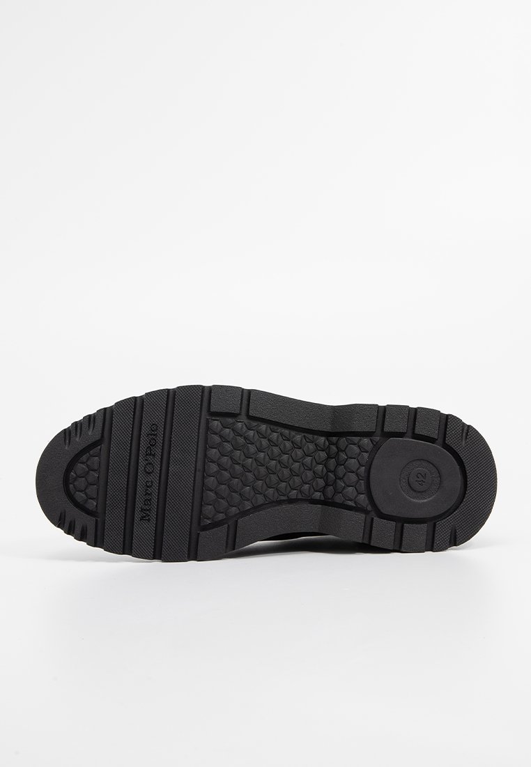 Czarna gumowa podeszwa buta z teksturowanym wzorem antypoślizgowym i okrąłym logiem. Płaski design z wypukłymi brzegami zwiększającymi przyczepność.