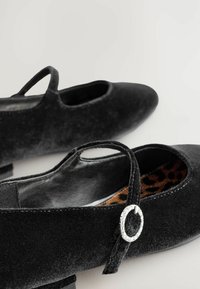 Baletă cu talpă din suede negru, cu brățară la glezna, având detaliu de cataramă rotundă din argint și interior cu imprimeu de leopard. Toc mic, textură moale.