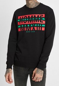 Czarny sweter z mocnym tekstem w czerwonych i zielonych paskach, na którym widnieje napis "HOMME MMXIII NEW YORK". Wykonany z miękkiego materiału, z prążkowanymi mankietami.