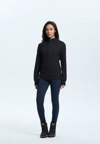 Svart zip-neck topp med långa ärmar, tillsammans med marinblå leggings och svarta snörboots. Slitstarkt tyg med en figurnära design.