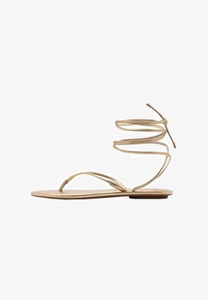 Guld flad sandal med tynde, spiralsnore omkring anklen, åben tå design og en minimalistisk sål. Har en glat, metallisk finish.