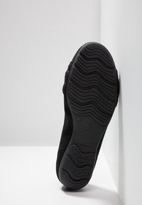 Chaussure noire en daim avec une semelle en caoutchouc texturé, présentant des motifs nervurés et une marque en relief ; conçue pour le confort et la stabilité.
