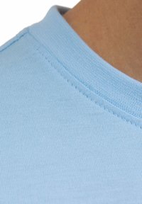 Jasnoniebieska bawełniana tkanina o textured powierzchni, z widocznym prążkowanym dekoltem i delikatnym detalem szwów.