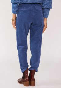 Pantaloni in corduroy blu con righe verticali, caratterizzati da una vestibilità comoda e orli arrotolati, abbinati a stivaletti alla caviglia con tacco marroni.