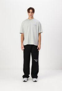 Gray cotton t-shirt with short sleeves and blue logo on the chest, paired with loose black sweatpants featuring a white graphic. Light sneakers.