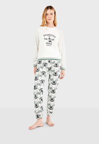 Weißer Pullover mit schwarzem Druck, der Sylvester den Kater zeigt, kombiniert mit Schlafanzughosen, die ein sich wiederholendes schwarz-weißes Cartoon-Muster aufweisen.