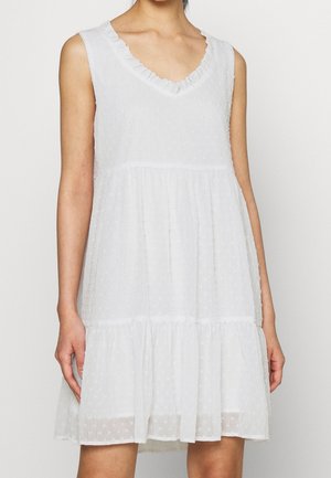 Biała sukienka bez rękawów z falbanianym dekoltem w kształcie litery V, teksturowaną tkaniną z drobnym wzorem w kropki oraz rozkloszowanym dołem z warstwowym zakończeniem.