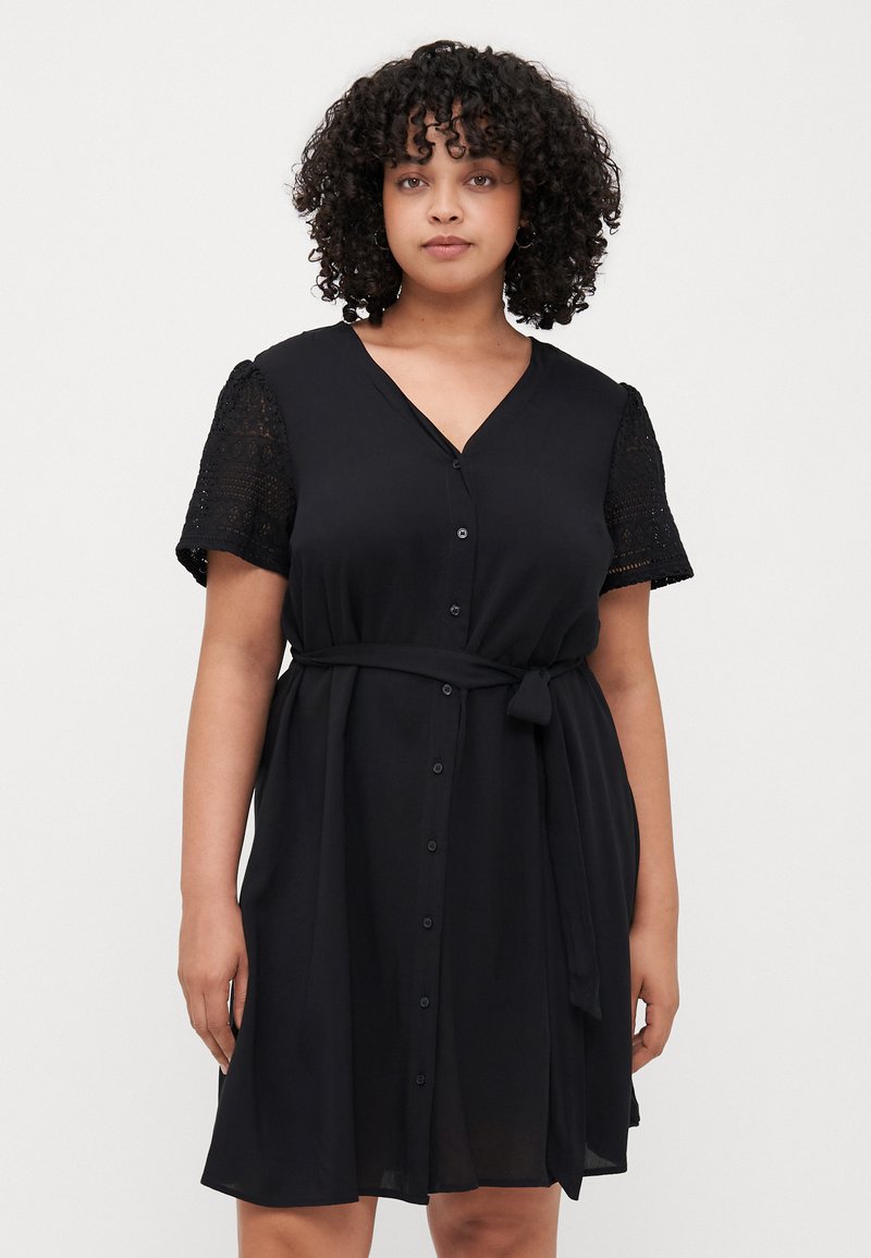 Black dress with a V-neck, short lace sleeves, and a tied waist. It features a button-down front and a flowy design.