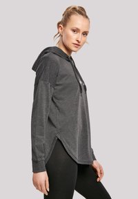 Sudadera gris con mangas largas, bolsillo canguro, capucha con cordón y dobladillo dividido. Tela suave y texturada con un ajuste relajado.