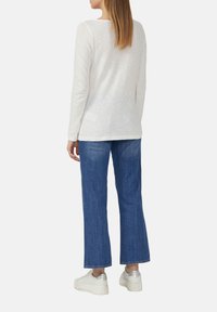 White long-sleeve shirt made of lightweight fabric, paired with blue wide-leg jeans and white sneakers with silver accents.