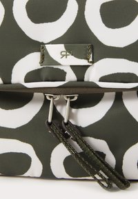 Green canvas bag with large white circular patterns. Features a zip closure with two silver hardware pulls and a small logo tag.