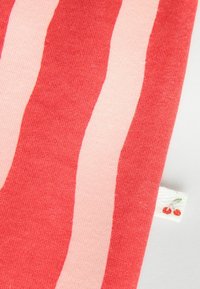 Piros és világos rózsaszín csíkos textil, puha tapintással. Az élen egy kis cseresznye mintás címke található.