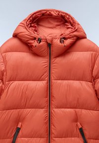 Gevoerde oranje jas met een capuchon, voorzien van een volledige ritssluiting aan de voorkant, zwarte ritssluitingaccenten en elastische toggles voor aanpassingen aan de capuchon.