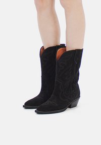 Cizme de cowboy din suede negru, cu broderie decorativă, vârf ascuțit și toc mic, păstrat. Interiorul prezintă o căptușeală contrastantă, de culoare maro.