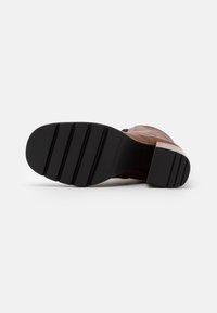 Botte en cuir marron avec une semelle noire texturée, présentant des motifs nervurés pour l'adhérence et un dessus lisse avec des détails de couture minimaux.