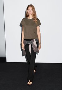 Oliwkowa, krótko rękawowa koszulka, w zestawieniu z czarnymi, szerokimi spodniami. Na talii związany jest brązowy i szary sweter w romby. Płaskie sandały.