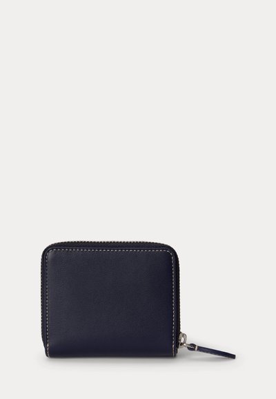 Portefeuille compact en cuir bleu marine avec coutures blanches visibles et fermeture éclair tout autour avec une languette en cuir sur fond blanc.
