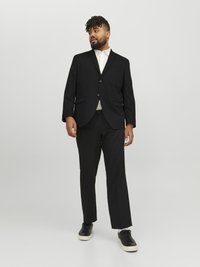 Black suit with a single-breasted jacket, two buttons, and notch lapels. Paired with a white shirt and black sneakers. Flat-front trousers.