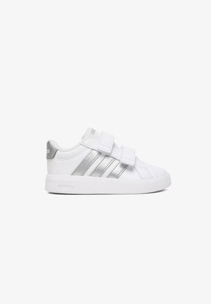 Sneaker Adidas bianca con strisce argentate, due cinturini in velcro e suola e linguetta del tallone con logo, mostrata su uno sfondo bianco uniforme.