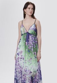 Maxi abito con stampa floreale in tonalità verde e viola, caratterizzato da una profonda scollatura a V, spalline sottili e un tessuto leggero e fluido.