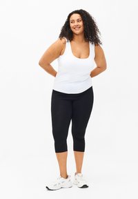 White tank top and black capri leggings, made from stretch fabric. Model wearing sports shoes; casual design with fitted silhouette.