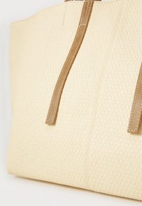 Beige geflochtene Tragetasche mit zwei braunen Ledergriffen und Nähten. Strukturierte Oberfläche mit einer festen Form und ohne zusätzliche Verzierungen.