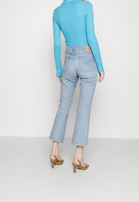 Jeans de tiro alto azul claro con pierna acampanada, combinados con una blusa ajustada de manga larga color turquesa y zapatos de tacón alto marrones con estampado.