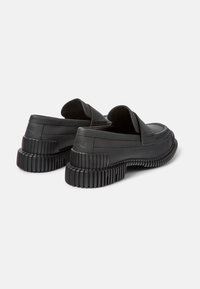 Svarta läderskor med rund tå, slip-on-design och en räfflad gummisula. Ingen synlig hårdvara eller mönster.