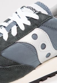 Baskets gris et vert foncé en daim et nylon avec des lacets blancs, des accents argentés et une semelle en caoutchouc dotée de découpes circulaires.