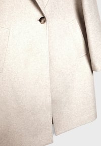Manteau en mélange de laine beige avec des revers structurés, fermeture à un bouton et deux poches plaquées, offrant une finition lisse et texturée.