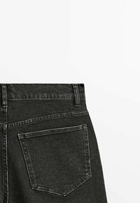 Vue arrière d'un jean en denim noir montrant la taille, les passants de ceinture et une seule poche arrière avec des coutures visibles.
