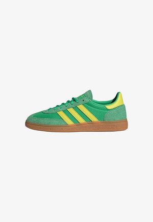 Grüne und gelbe Sneaker aus Wildleder und Mesh-Materialien, mit einer Sohle aus Gummi und drei gelben Streifen an der Seite.