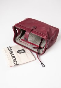 Burgundy leather bag with a rectangular shape, zip closure, striped interior, and a fabric pouch featuring a logo and text.
