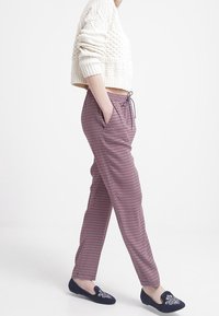 Geweven cropped trui in crème, gecombineerd met gestreepte elastische taillebroek in kastanjebruin met witte details, en marineblauwe instap schoenen met versieringen.