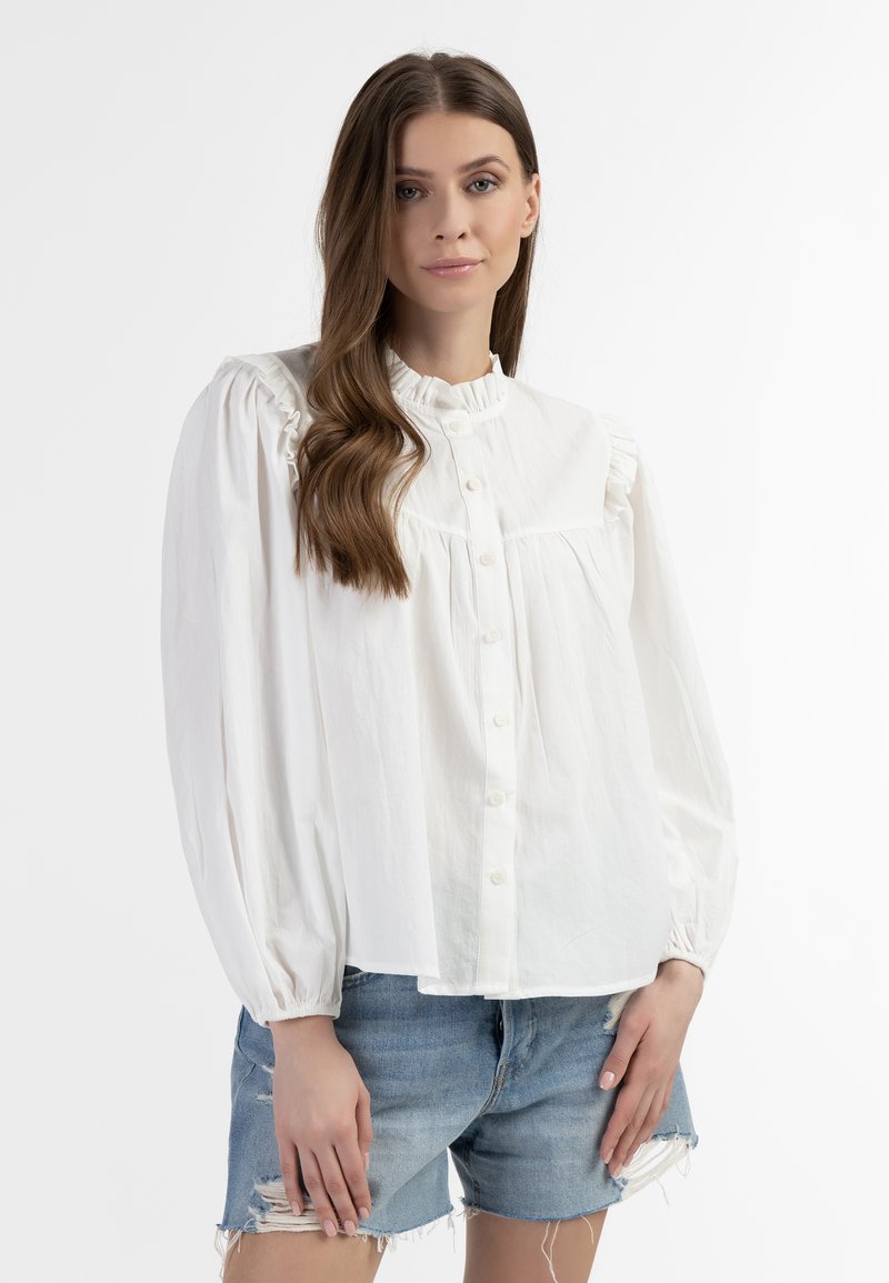 Blusa di cotone bianca con colletto a volant, chiusura a bottoni e maniche a sbuffo, abbinata a pantaloni shorts in denim strappato.