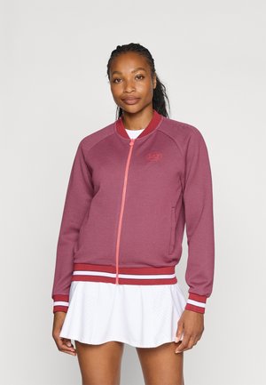 Giacca con zip frontale di colore bordeaux con accenti rosa a contrasto. Presenta polsini e orlo a coste con strisce bianche. Tessuto liscio, vestibilità atletica.