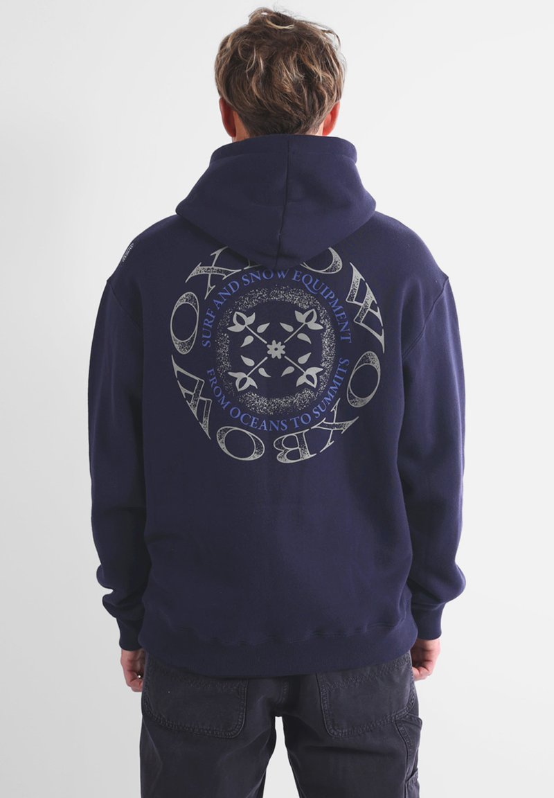 Hoodie en bleu marine avec un grand graphique circulaire au dos, comprenant du texte et des éléments floraux, fabriqué dans un tissu doux avec une coupe décontractée.