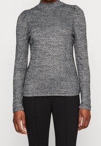 Haut gris à manches longues texturé avec un col montant et des épaules légèrement bouffantes, présentant un motif en maille côtelée et une silhouette ajustée.