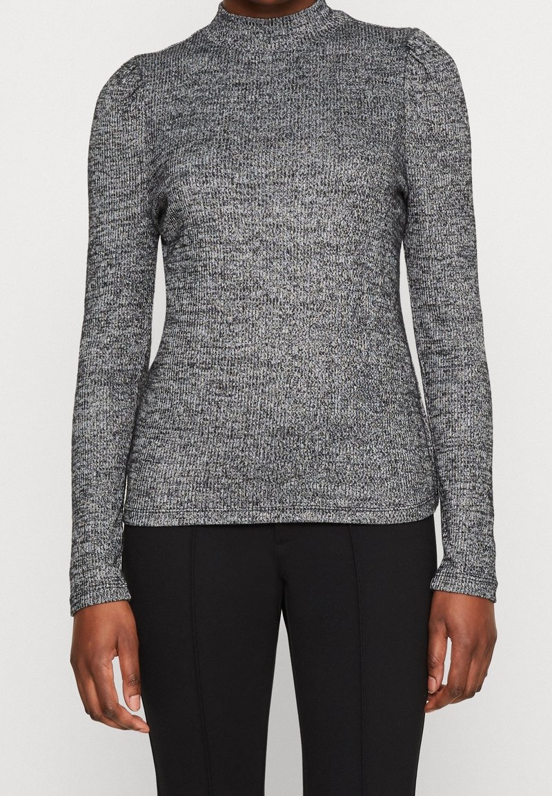 Haut gris à manches longues texturé avec un col montant et des épaules légèrement bouffantes, présentant un motif en maille côtelée et une silhouette ajustée.