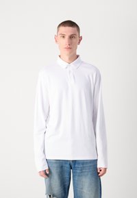 Langermet hvit polo med krage, med knappefeste og en ensfarget tekstur. Kombinert med lys blå slitte jeans.