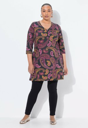 Tunique noire avec un motif paisley vibrant en rose et jaune, manches trois-quarts, associée à des leggings noirs et des chaussures plates métalliques.