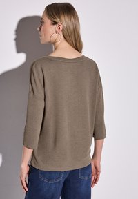 Olivově zelený volný dlouhý rukáv s kulatým výstřihem a texturovanou tkaninou, v kombinaci s modrými džíny, zobrazený zezadu.