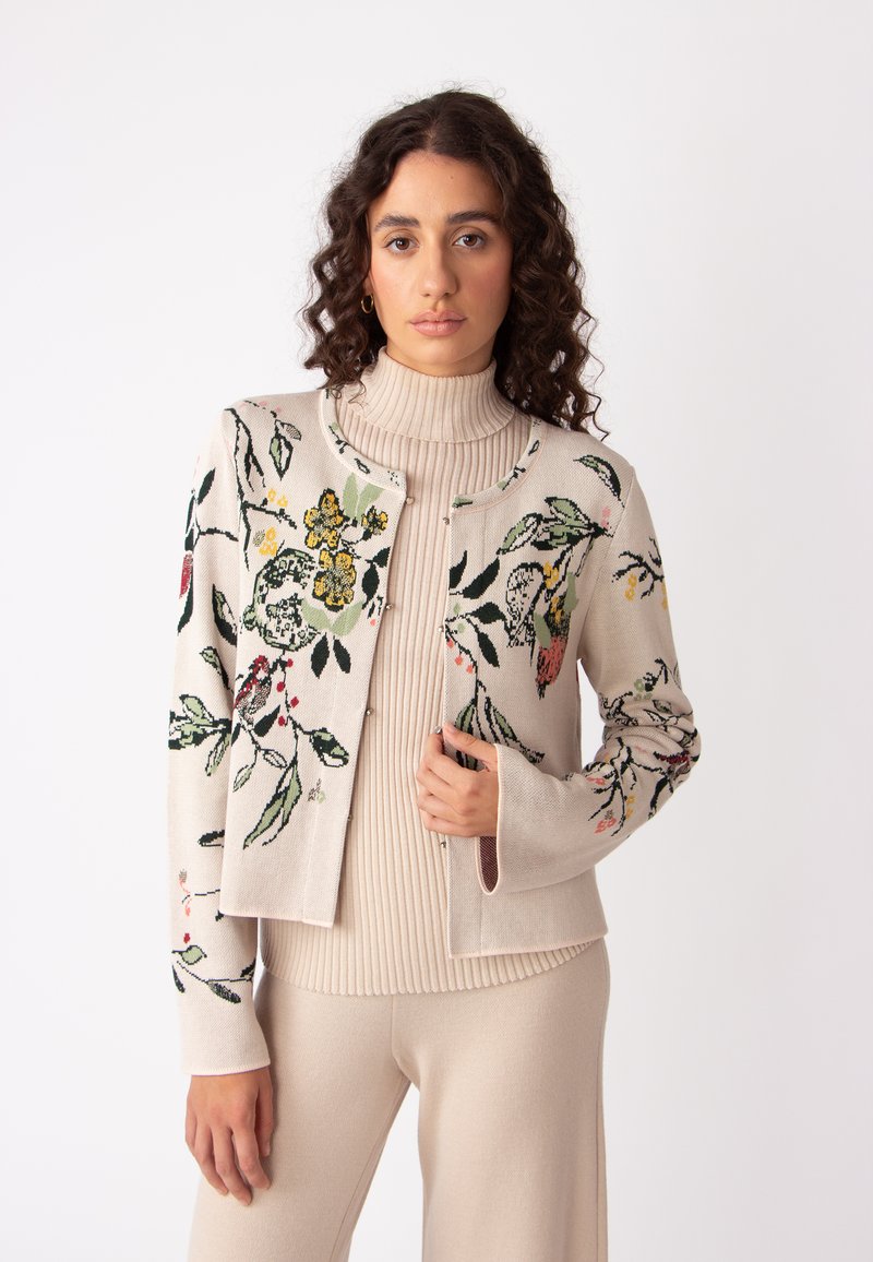 Gebreide cardigan in crème met florale borduursels in groen, geel en roze. Heeft een ronde halslijn en aansluitende mouwen.