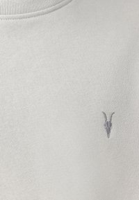 Maglione grigio chiaro con scollatura rotonda, caratterizzato da un sottile design ricamato di teschio di capra in grigio scuro nella zona del petto. Texture liscia.