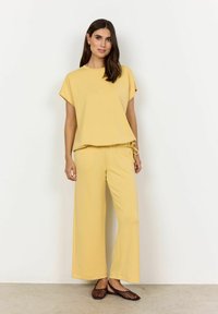 Gelbes Loungewear-Set mit einem boxy kurzen Oberteil und weiten Hosen mit verstellbarem Kordelzug. Glatter Stoff mit minimaler Verzierung.
